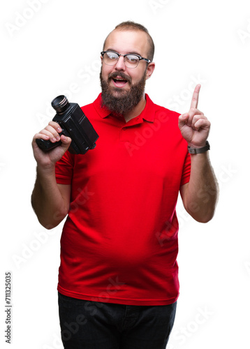 Young caucasian hipster man filmming using retro video camera over isolated background surprised with an idea or question pointing finger with happy face, number one
