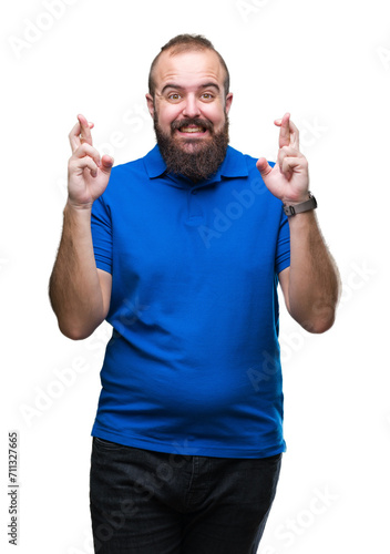 Young caucasian hipster man wearing blue shirt over isolated background smiling crossing fingers with hope and eyes closed. Luck and superstitious concept.