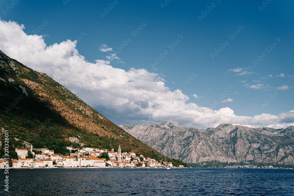 Ancient houses with red roofs and a church bell tower at the foot of the mountains. Perast, Montenegro