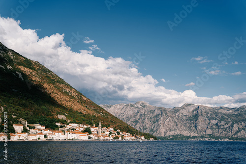 Ancient houses with red roofs and a church bell tower at the foot of the mountains. Perast, Montenegro