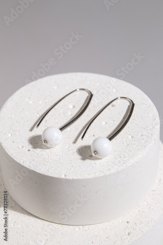 Two silver earrings with white agate on a concrete podium on podium. Beautiful accessories for women. An elegant jewelry gift or a gift for a birthday or Valentine s Day.