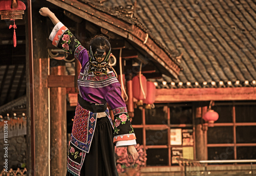 a young girl in a Chinese national dress, wearing a dragon mask, against the background of national buildings of houses, hanging red fanariks photo