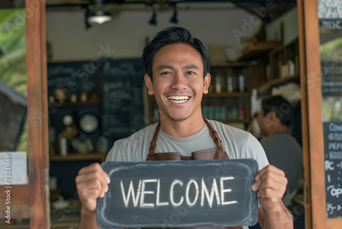cheerful Asian barista holding the welcome sign in the cafe photo