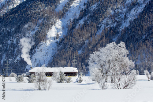 Winter landscape with frozen trees and snow-covered houses in Alps mountains