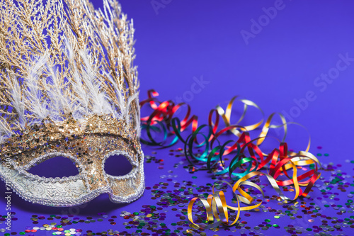 Fototapeta Naklejka Na Ścianę i Meble -  Golden Mardi Gras or carnival face mask on a purple background with colored tinsel and confetti. Selective focus.Venice Carnival.Carnival.