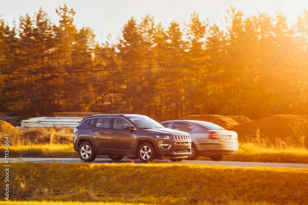 A subcompact SUV car explores the scenic countryside with a stunning sunset and alpine mountains in the background.