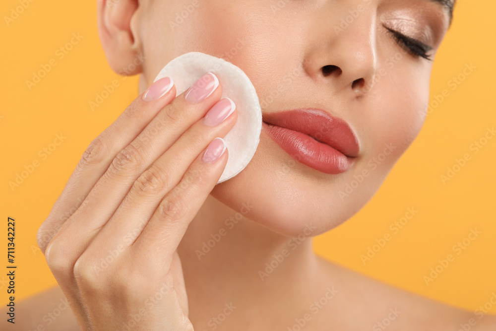 Beautiful woman removing makeup with cotton pad on orange background, closeup Beautiful woman removing makeup with cotton pad on orange background, closeup