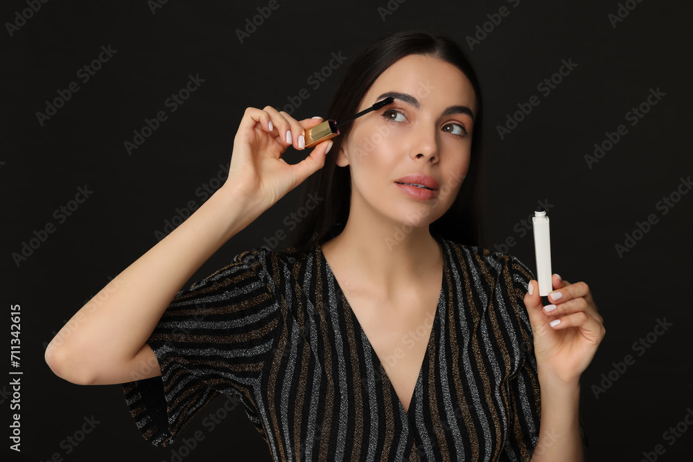 Obraz premium Beautiful young woman applying mascara on black background