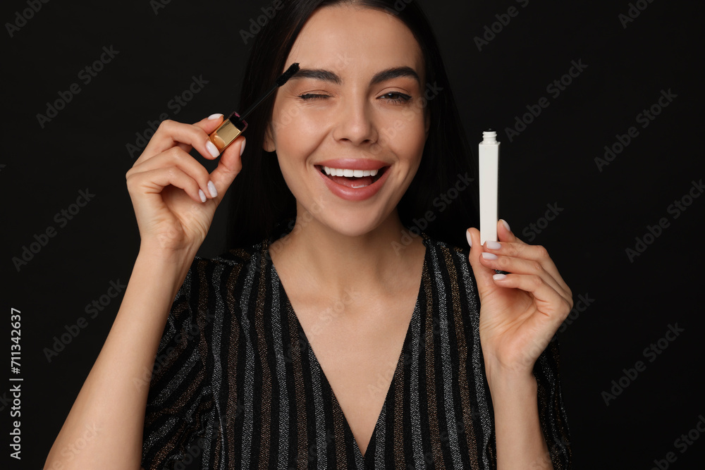 Obraz premium Beautiful young woman applying mascara on black background