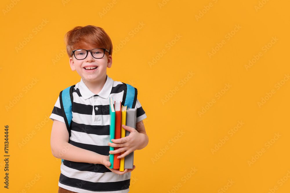 Happy schoolboy with backpack and books on orange background. Space for text Happy schoolboy with backpack and books on orange background. Space for text