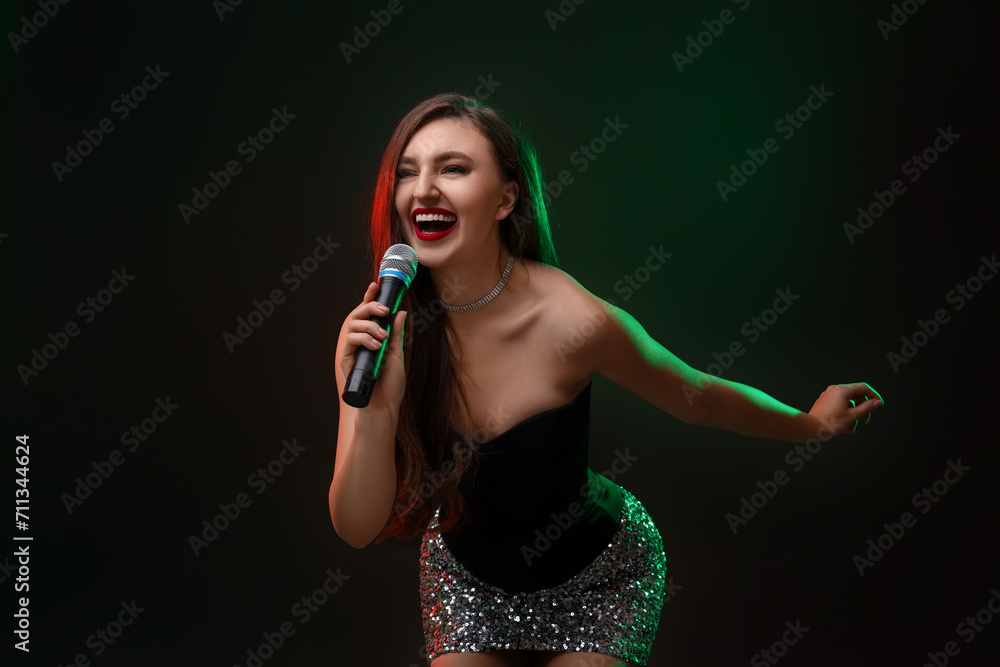 Emotional woman with microphone singing in color lights on dark background Emotional woman with microphone singing in color lights on dark background