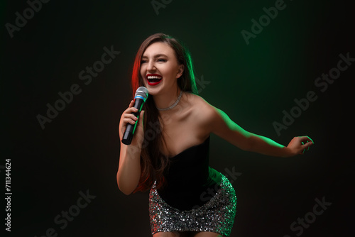 Emotional woman with microphone singing in color lights on dark background