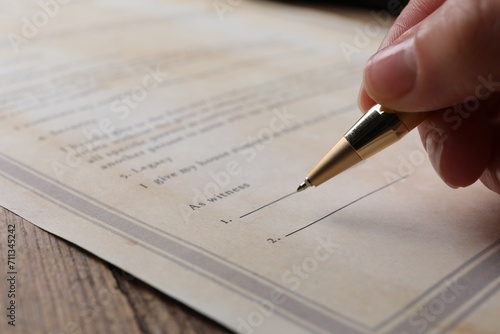 Woman signing Last Will and Testament at wooden table, closeup photo