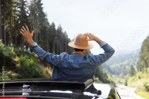 Enjoying trip. Man leaning out of car roof outdoors, back view