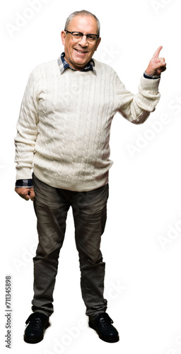 Handsome senior man wearing glasses and winter sweater with a big smile on face, pointing with hand and finger to the side looking at the camera.