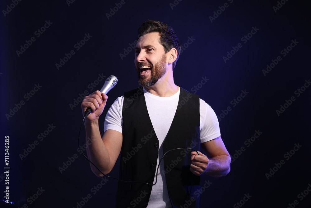 Naklejka premium Handsome man with microphone singing on dark blue background