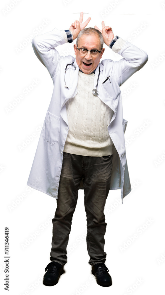 Handsome senior doctor man wearing medical coat Posing funny and crazy with fingers on head as bunny ears, smiling cheerful Handsome senior doctor man wearing medical coat Posing funny and crazy with fingers on head as bunny ears, smiling cheerful