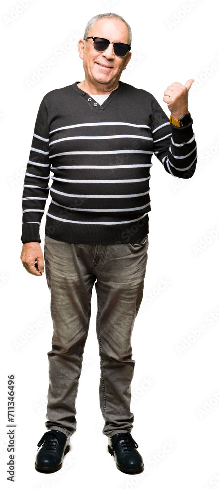 Handsome senior man wearing winter sweater and sunglasses smiling with happy face looking and pointing to the side with thumb up. Handsome senior man wearing winter sweater and sunglasses smiling with happy face looking and pointing to the side with thumb up.