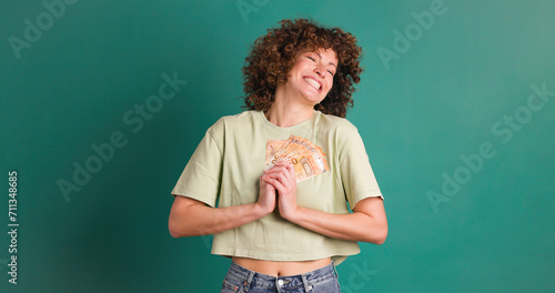 Cheerful woman showing Euro banknotes in green studio © DMegias
