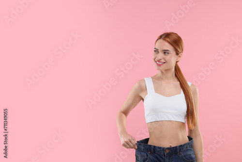 Slim woman wearing big jeans on pink background, space for text. Weight loss