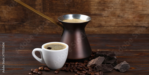 Turkish coffee. Cezve and cup with freshly brewed beverage, coffee beans and chocolate on wooden table. Banner design