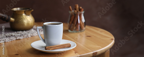 Turkish coffee. Cup of freshly brewed beverage, cinnamon and cezve on wooden table. Banner design with space for text