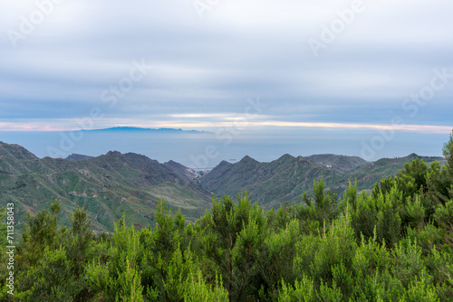 Beautiful landscape with a bush in the foreground, mountains, a boat and the island of Gran Canaria in the background and the Atlantic Ocean with a golden sky, in the Anaga natural park, Tenerife