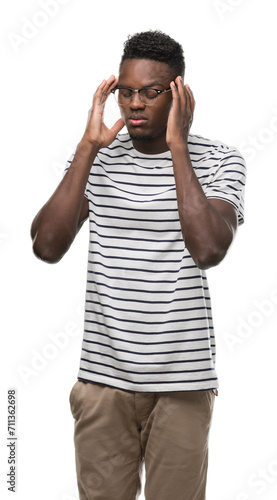 Young african american man wearing glasses and navy t-shirt with hand on head for pain in head because stress. Suffering migraine.