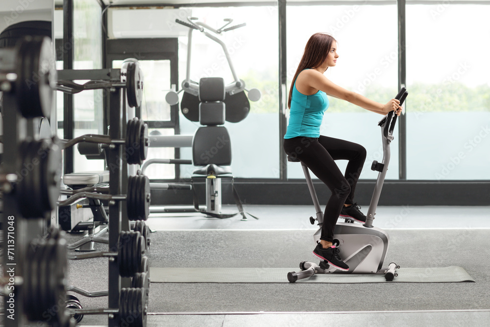 Fototapeta premium Young female riding a stationary bike at a gym