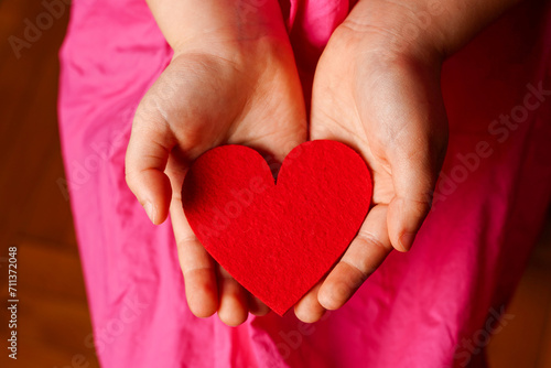 Child s hands holding bright red heart on pink background