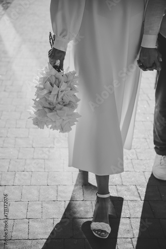 Bride and groom walk outdoors. Bride and groom hold hands and walking on the street. Closeup. Details of wedding moments. Newlyweds together. Down view. Black and white photo. Couple hands.