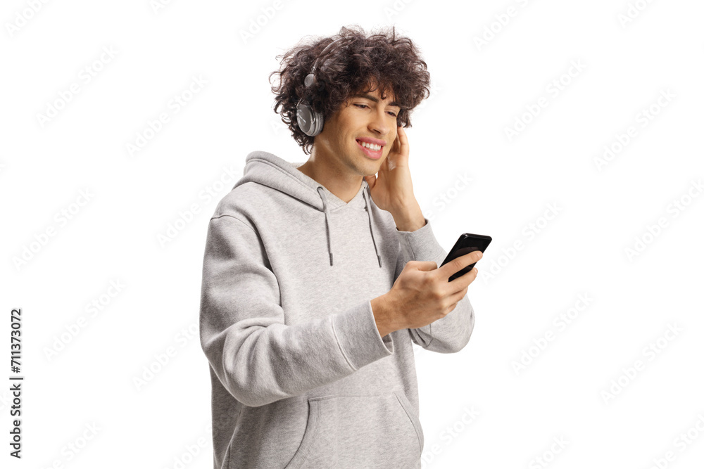 Guy with curly hair holding a smartphone and listening to music on headphones