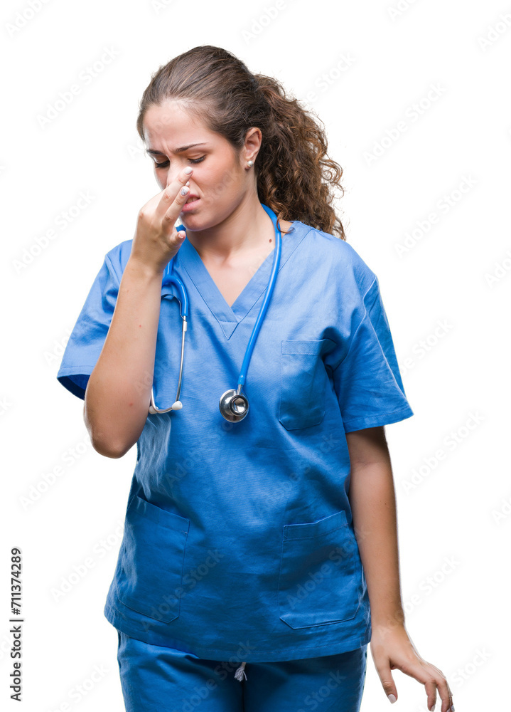 Young brunette doctor girl wearing nurse or surgeon uniform over isolated background smelling something stinky and disgusting, intolerable smell, holding breath with fingers on nose. Young brunette doctor girl wearing nurse or surgeon uniform over isolated background smelling something stinky and disgusting, intolerable smell, holding breath with fingers on nose.