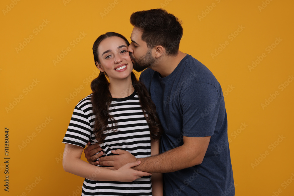 Man kissing his smiling girlfriend on orange background Man kissing his smiling girlfriend on orange background