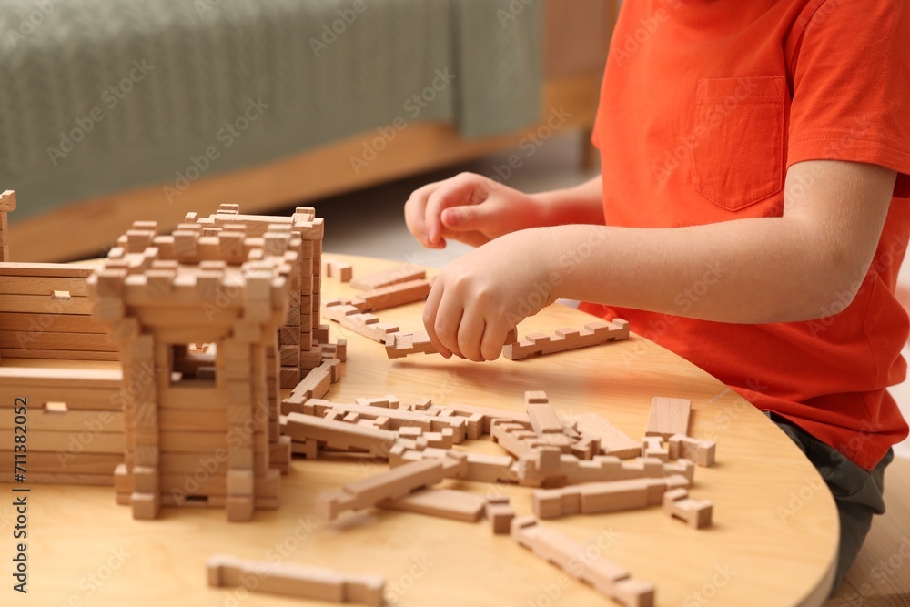 Little boy playing with wooden construction set at table in room, closeup. Child's toy Little boy playing with wooden construction set at table in room, closeup. Child's toy