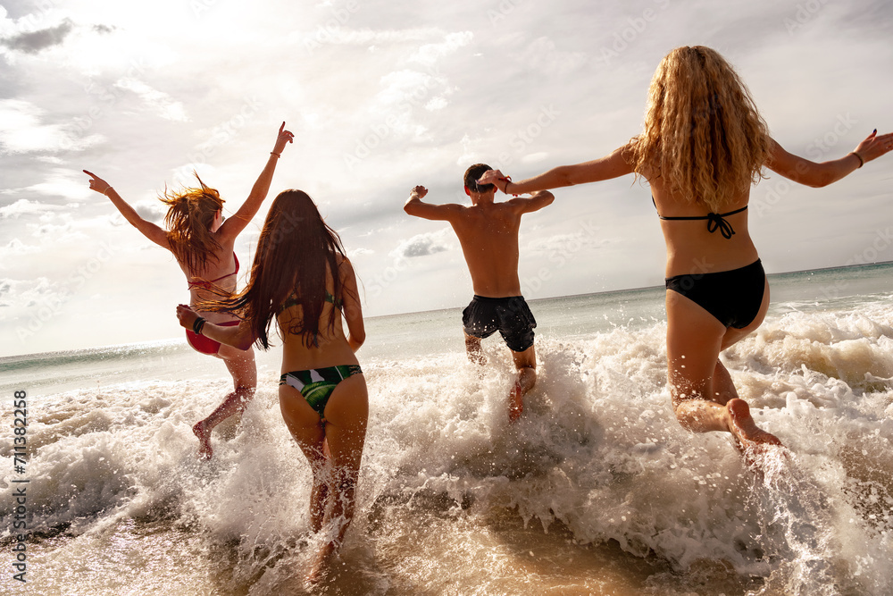 Fototapeta premium Four happy young friends are having fun and runs to sunset sea beach. Tropical vacations concept
