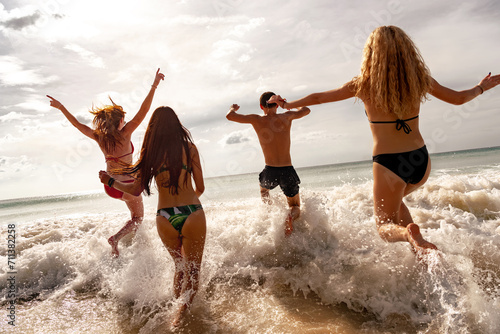 Four happy young friends are having fun and runs to sunset sea beach. Tropical vacations concept