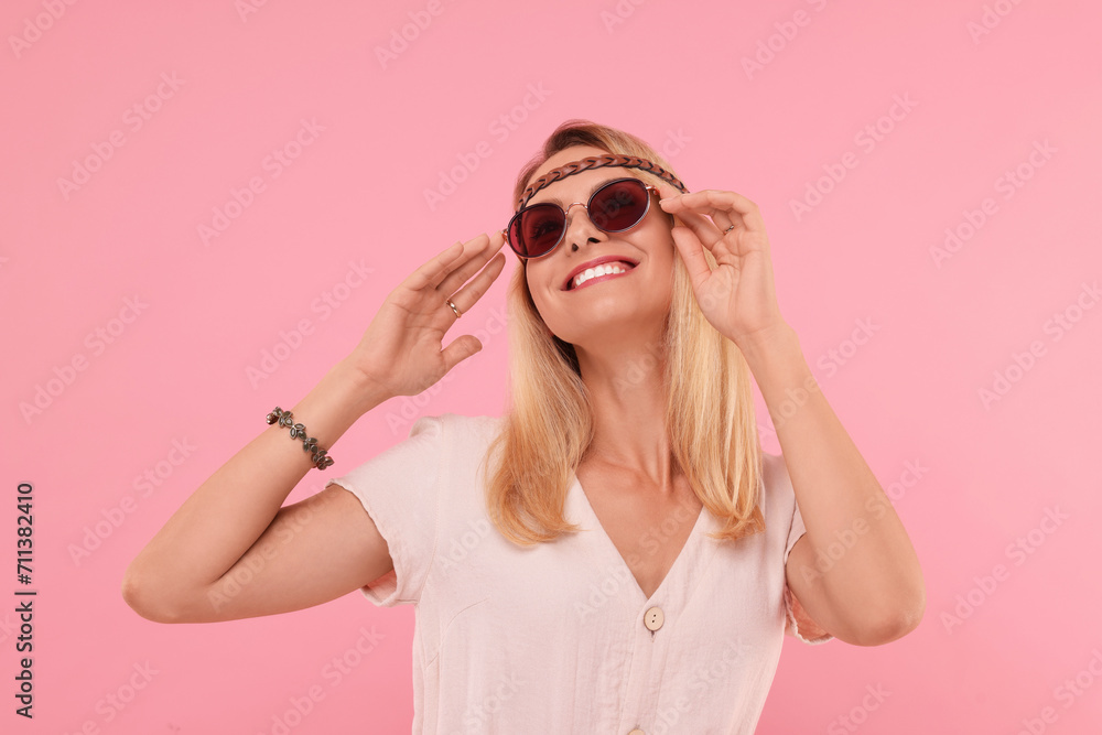 Portrait of smiling hippie woman in sunglasses on pink background Portrait of smiling hippie woman in sunglasses on pink background