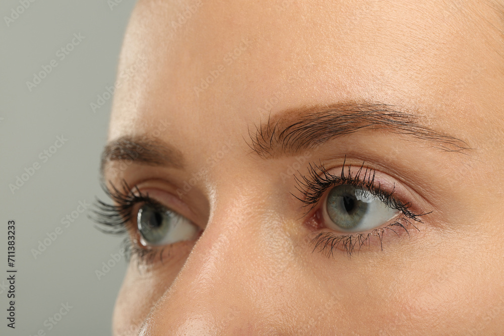 Fototapeta premium Woman with long eyelashes after mascara applying against grey background, closeup