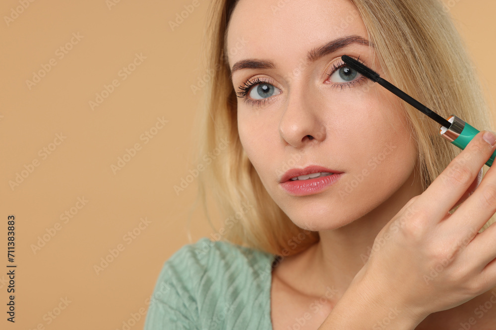 Beautiful woman applying mascara on beige background, closeup. Space for text Beautiful woman applying mascara on beige background, closeup. Space for text