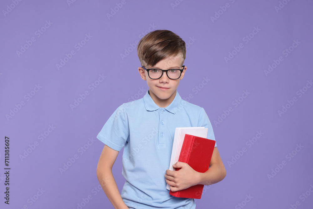 Fototapeta premium Cute schoolboy in glasses holding books on violet background