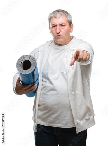 Handsome senior man holding yoga mat over isolated background pointing with finger to the camera and to you, hand sign, positive and confident gesture from the front