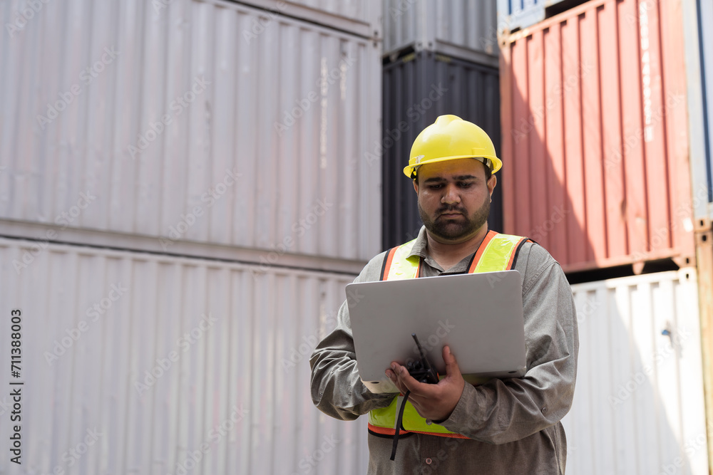Portrait of male container yard worker loading containers box with laptop computer at commercial dock site. Male supervisor checking container at container terminal yard Portrait of male container yard worker loading containers box with laptop computer at commercial dock site. Male supervisor checking container at container terminal yard