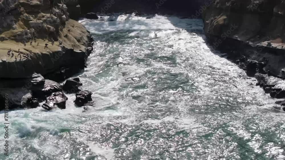 Sun shining on crashing waves against rocks in a cove on a beach in La Jolla California, aerial pullback
