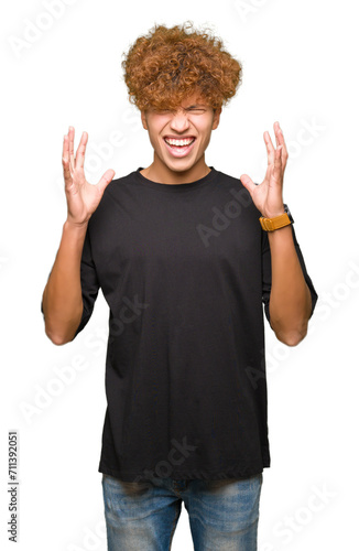 Young handsome man with afro hair wearing black t-shirt crazy and mad shouting and yelling with aggressive expression and arms raised. Frustration concept.