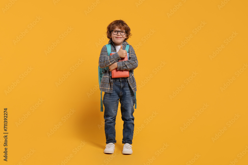 Happy schoolboy with backpack and books on orange background Happy schoolboy with backpack and books on orange background