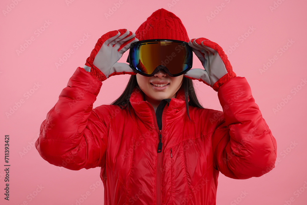 Happy woman in winter sportswear and goggles on pink background Happy woman in winter sportswear and goggles on pink background