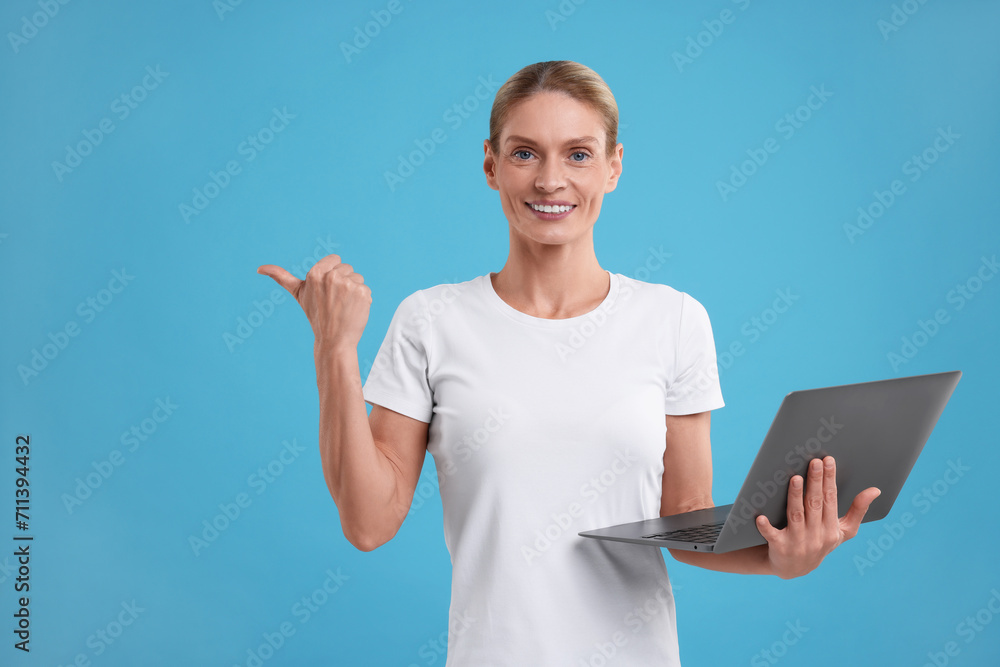 Special promotion. Smiling woman with laptop pointing at something on light blue background Special promotion. Smiling woman with laptop pointing at something on light blue background