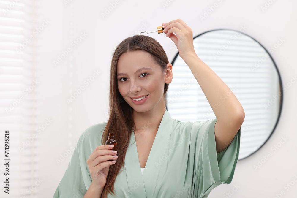 Beautiful woman applying serum onto hair indoors Beautiful woman applying serum onto hair indoors