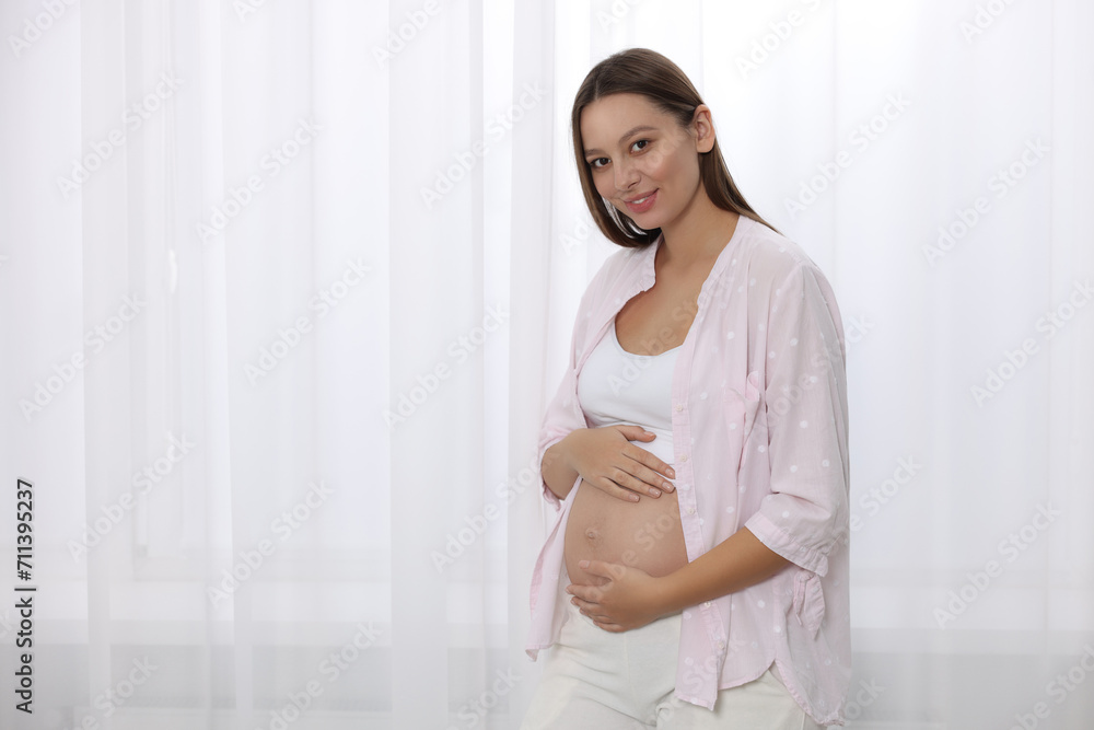 Beautiful pregnant woman near window indoors, space for text Beautiful pregnant woman near window indoors, space for text